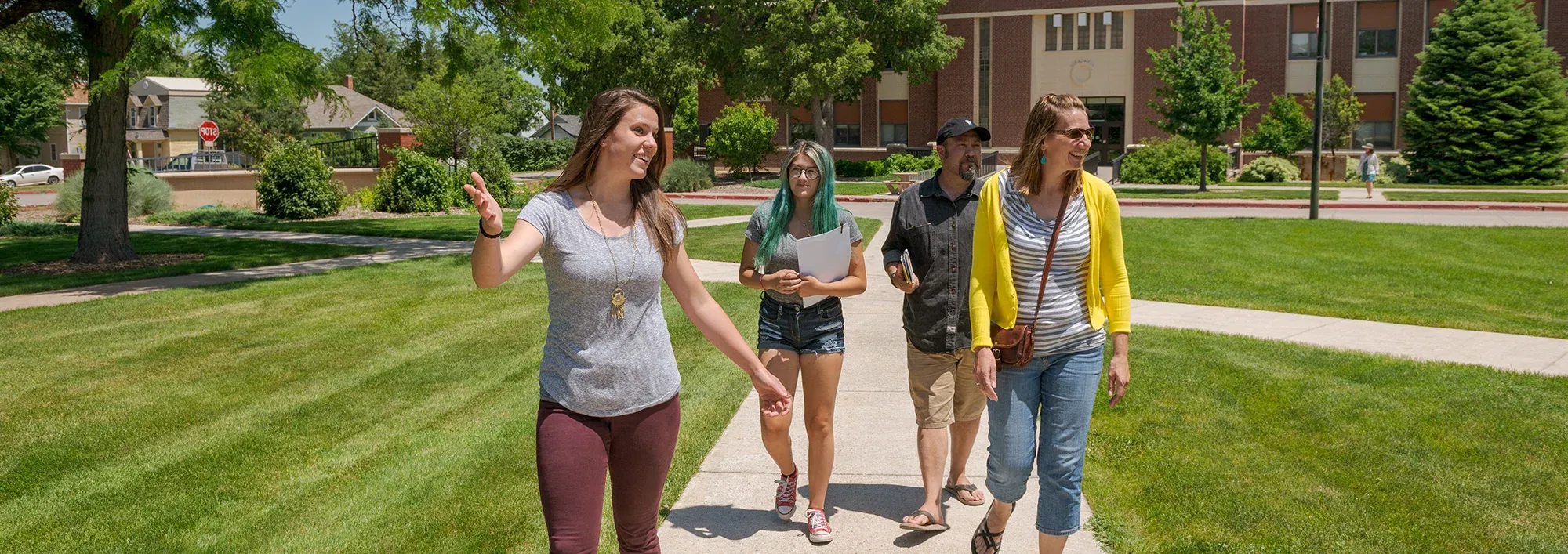 Student tour guide leading a family across a campus green space